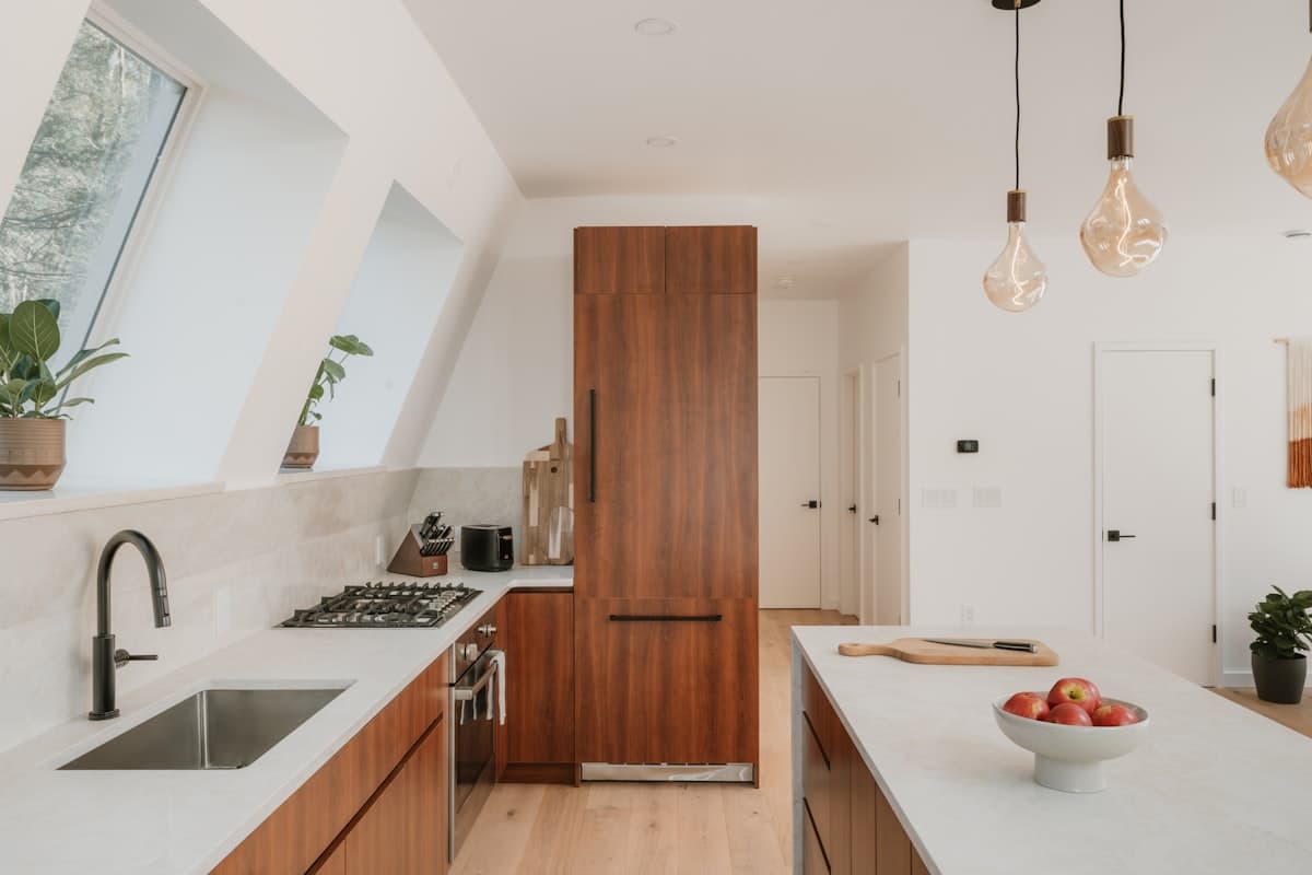 Cocina con mesón blanco, gabinetes de madera y lámparas colgantes