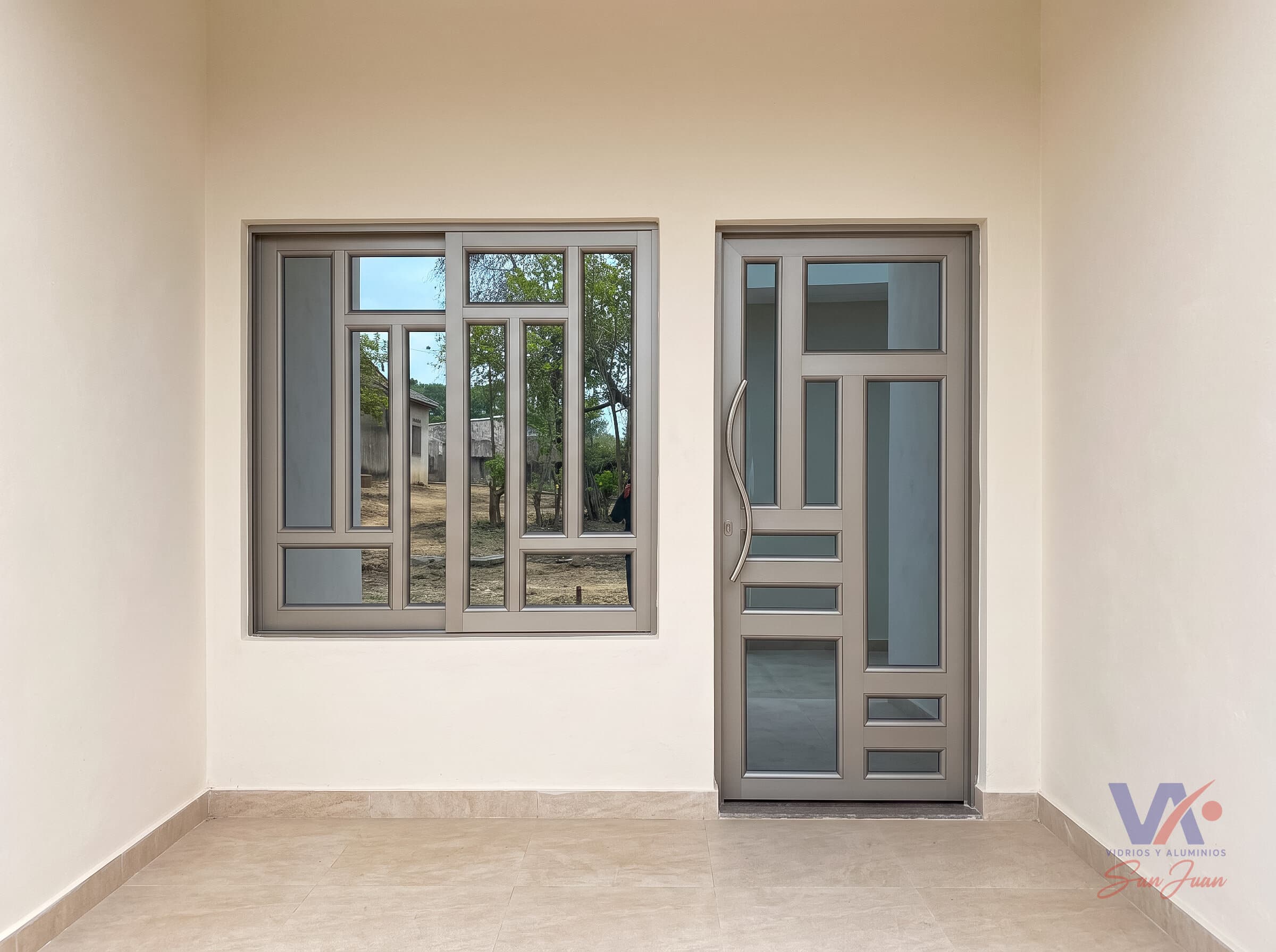 Ventana corrediza y puerta de aluminio color gris plata con vidrios, instaladas en la entrada de una vivienda