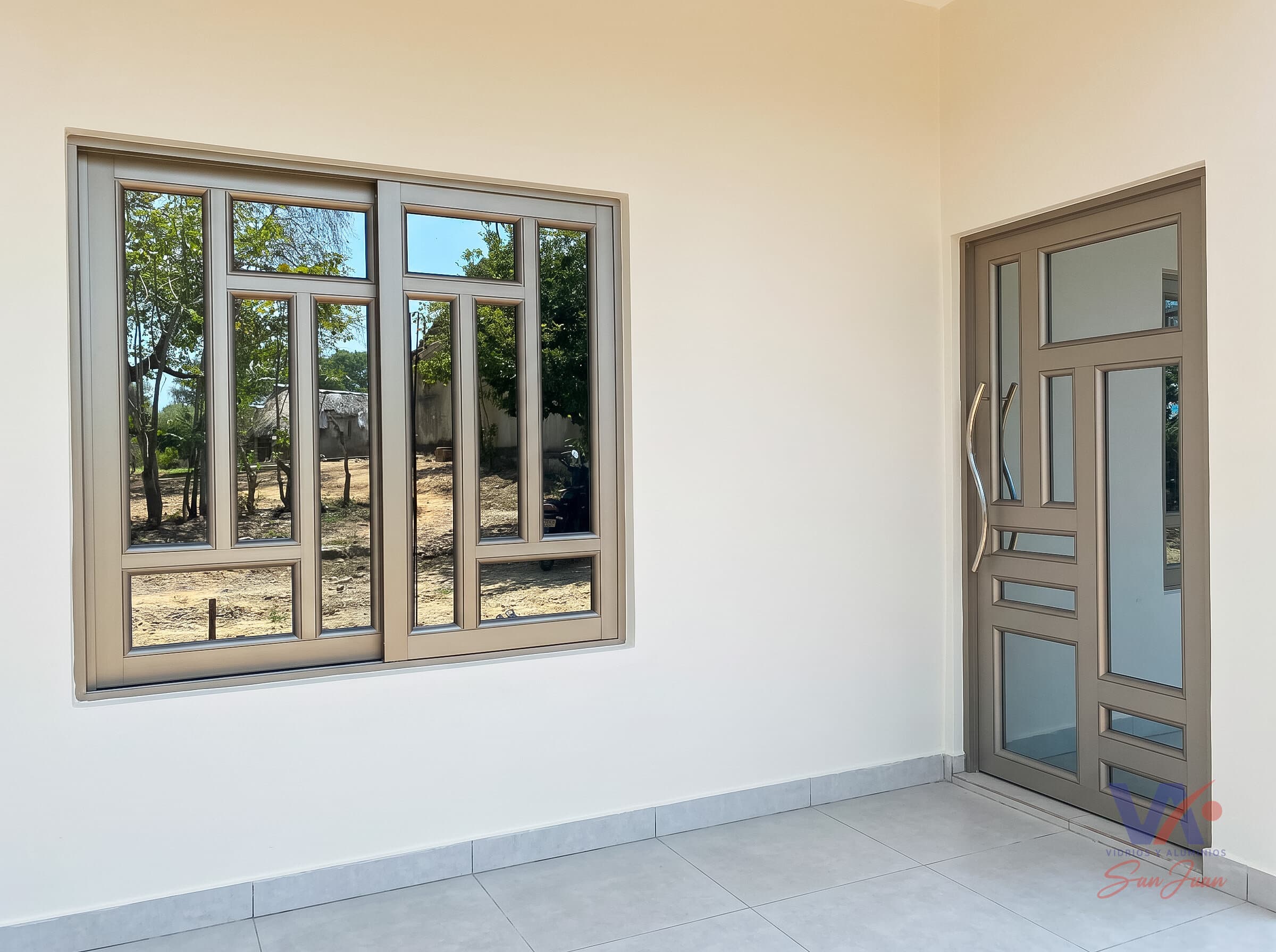 Ventana corrediza de aluminio color gris plata con vidrios en cuadros, junto a una puerta del mismo diseño