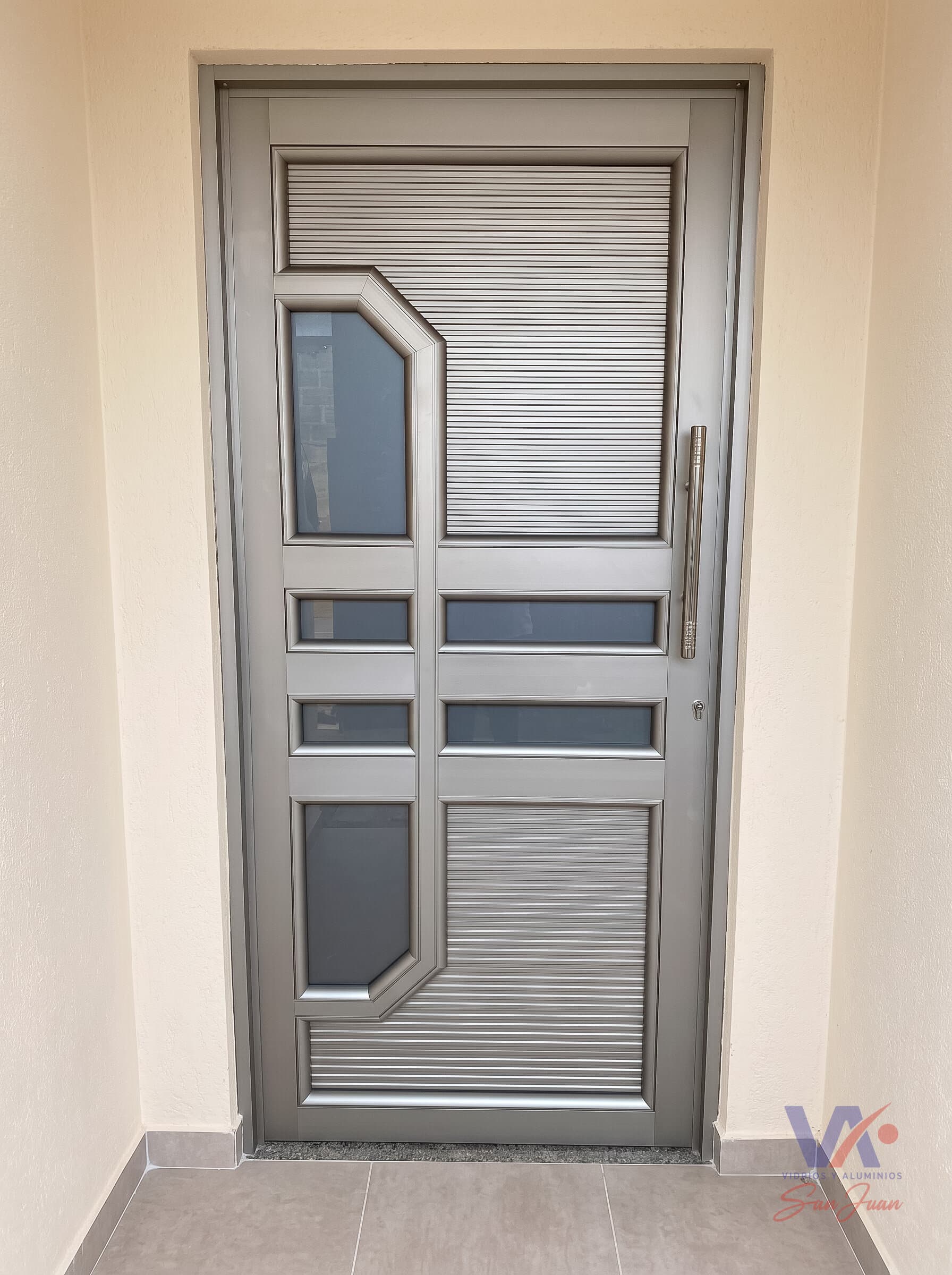 Puerta de aluminio color gris plata con paneles acanalados y vidrios de corte diagonal, instalada en una entrada