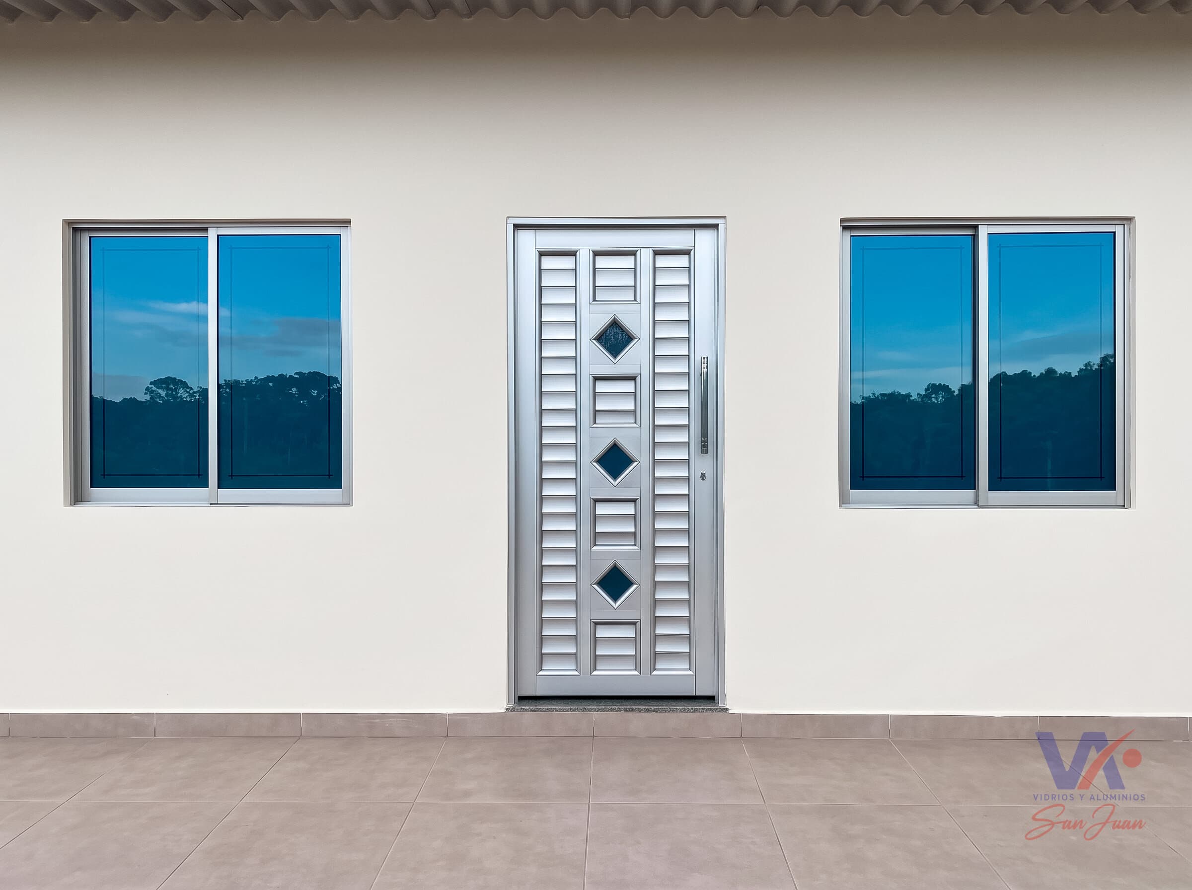 Dos ventanas corredizas de aluminio color gris plata a los lados de una puerta con vidrios en rombo