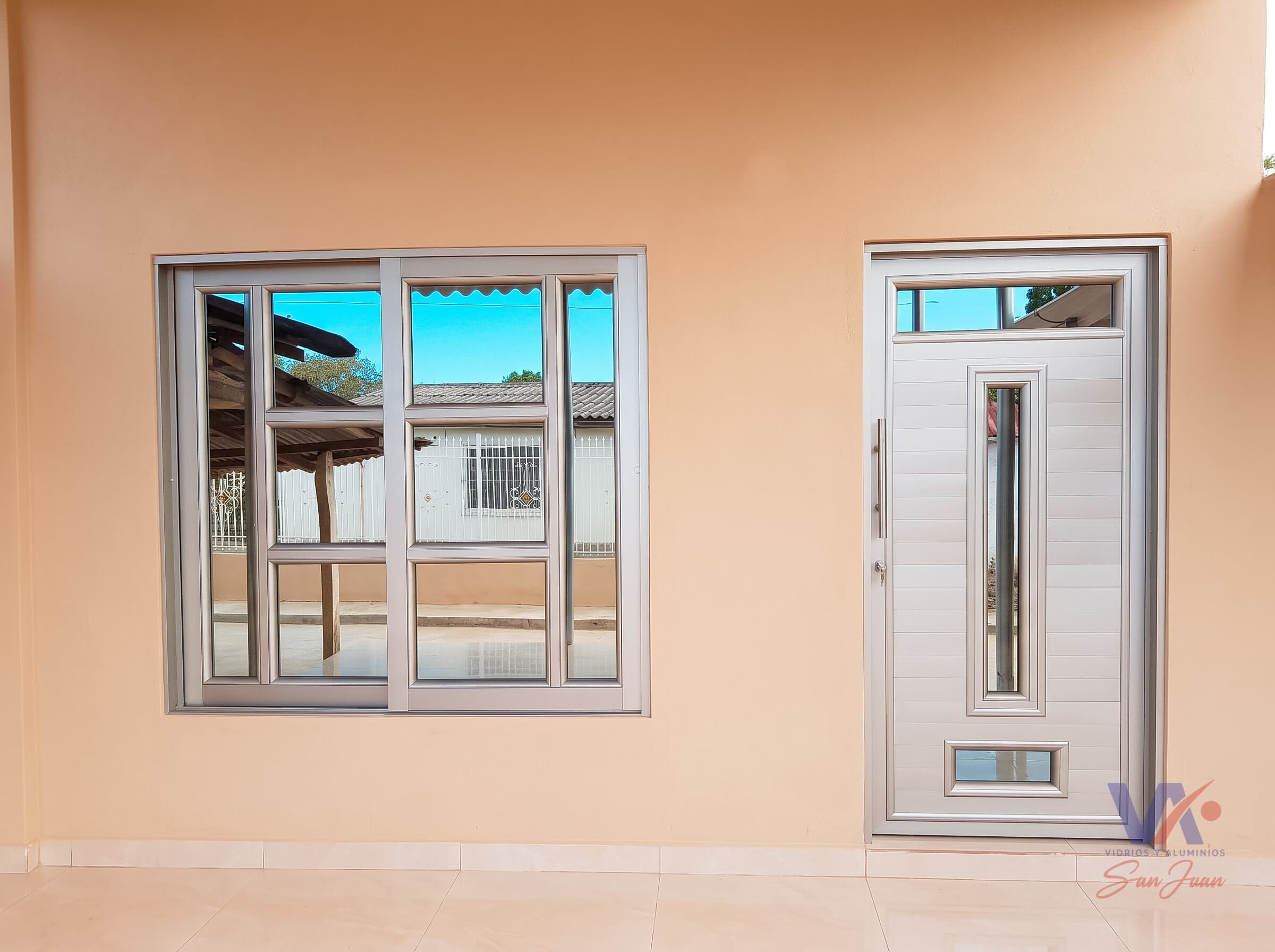 Ventana corrediza de aluminio con vidrios divididos, junto a una puerta con una franja vertical de vidrio