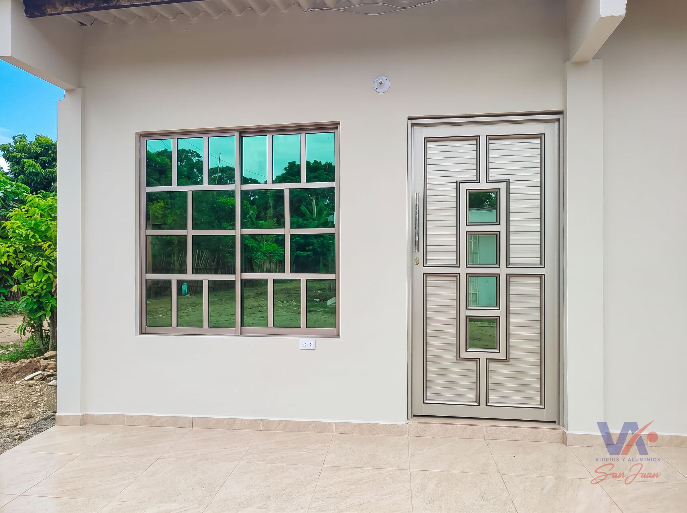 Ventana corrediza de aluminio con vidrios en cuadrícula, junto a una puerta con paneles acanalados